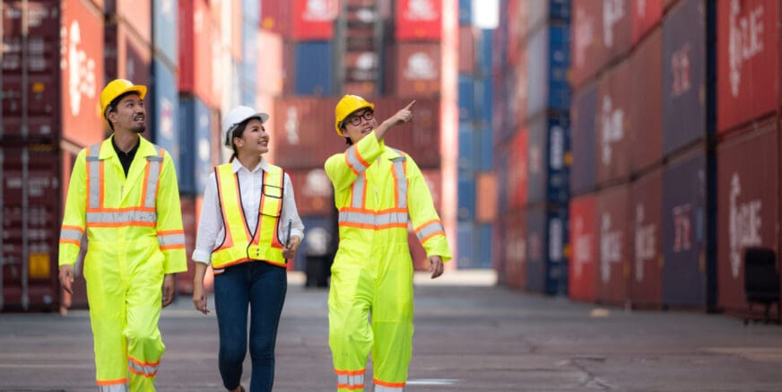 Group of engineers working with laptop in the container yard. This is a freight transportation and distribution warehouse.